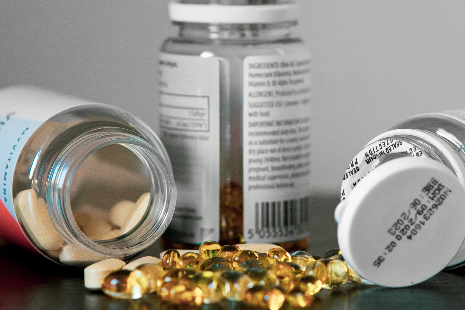 Open supplement bottles with tablets and softgels on a table